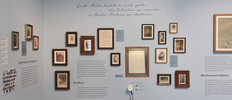Wandausschnitt der Ausstellung "Kunst und Leben – Leben und Kunst" mit kleinformatigen gerahmten Schwarz-Weiß-Fotografien und Wandtexten